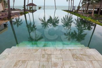 Wide marble steps go down in pool. Smooth water of pool reflects high picturesque palm trees in a beach of Andaman sea
