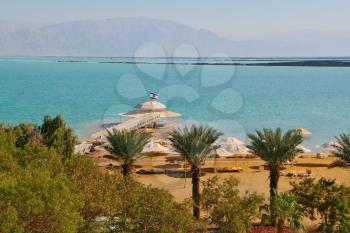 Solar beach on the Dead Sea. Wonderful warm day in December. A beach arbor and palm trees ashore