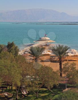 Solar beach on the Dead Sea. Wonderful warm day in December. A beach arbor, palm trees and hammocks ashore