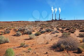 Three large pipes in the desert of red sandstone smoke in the blue sky
