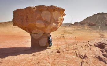 The woman-tourist in red desert near to huge mushroom from sandstone