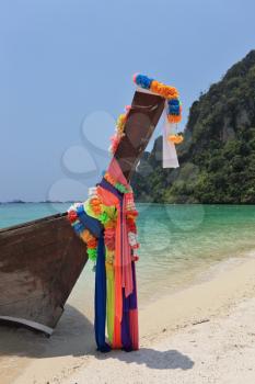 The native boat decorated with silk tapes is moored in thin gentle beach sand. Island Phi-Phi, Thailand
