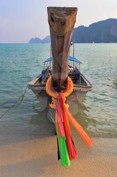 Orange Thai tourist boat moored on the beach. Bow is decorated with colorful and bright silk scarves