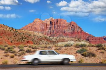 A white car passes at high speed on the road to Zion National Park. Sunset