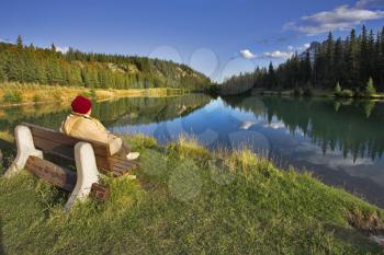  Fine lake in mountains of Canada and the woman having a rest on a bench on coast