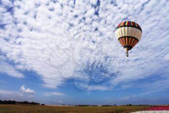The picturesque bright balloon with a passenger basket flies by over spring blossoming fields
