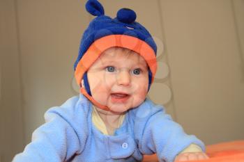 Charming baby boy with blue eyes in a blue hat with ears trying to crawl