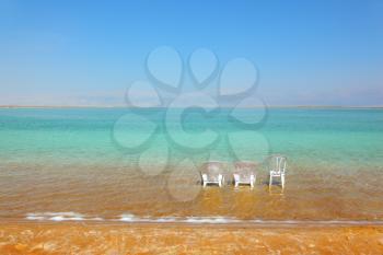 White beach armchairs and a chair in the warm clear water beach. Beach at the Dead Sea in May