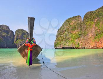 Scenic green islands of Thailand coast. Emerald sea and fine white sand. On the beach approached by a native boat for tourists, decorated with a red silk scarf