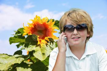 Field of sunflowers. Beautiful blond boy with sunglasses talking on cell phone