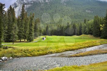 A field for a golf and rather shallow mountain small river in mountains