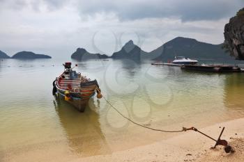 Thai Longtal boat moored on a sandy beach with an anchor. Picturesque bay on the island surrounded by islands
