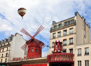 Big balloon flies over the Parisian cabaret Moulin Rouge. Red Tower, mill wings and the words Moulin Rouge.