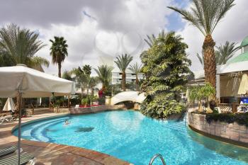 The ornate pool in an environment of palm trees, awnings and beach plank beds