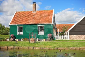 An ancient Dutch village. Cute little house with a red roof, water well and a river with floating ducks