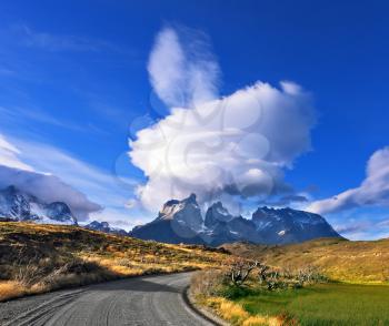 Amazing sunset in the Chilean Patagonia. Fabulous clouds over cliffs Los Kuernos in national park Torres del Paine. The dirt road leads to the mountain range