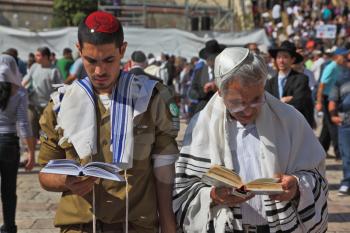 Jerusalem - October 16: The Holy Western Wall of the Temple. Jewish family - the father of religious clothing and his son, a soldier in uniform, praying in the square near the Wailing Wall in Sukkot, 