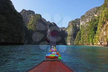 The Thai excursion boat swims in a picturesque bay. The boat nose is decorated by multi-colored and bright silk scarfs