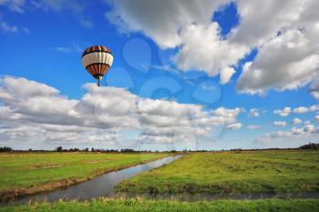 Bright striped balloon flies over the flat plain that is crossed by narrow water channels