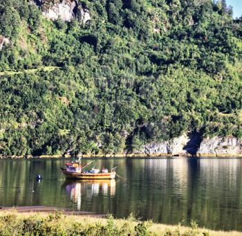  Charming quiet backwater in the river next to the road. Red fishing boat reflected in the smooth surface of the water.  Carretera Austral - the famous road in the Chilean Patagonia