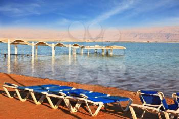 The Dead Sea, the blue beach chairs waiting for tourists. Beautiful sunny day at a beach resort