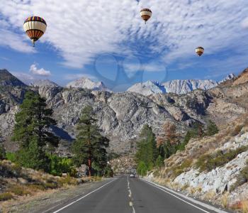 Huge balloons with the passenger basket flying over the magnificent American roads in the mountains
