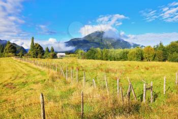 Green field fenced low fence. Mountain range is visible in the distance. Countryside in Chilean Patagonia
