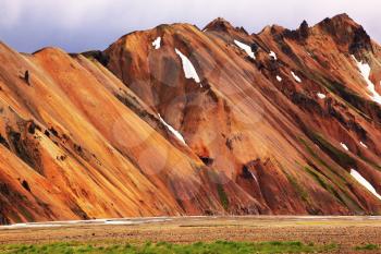 Smooth orange rhyolite mountains in Landmannalaugar nature reserve. In the hollows is last year's snow