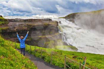  On mountain slope the woman delighted looks at a boiling chasm. Powerful Gullfoss in Iceland. 