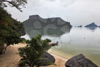 Thai Longtail boat moored on a sandy beach with an anchor. Picturesque bay on the island surrounded by islands. Foggy morning after a heavy storm

