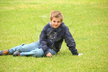 The beautiful boy has a rest on a green lawn in park