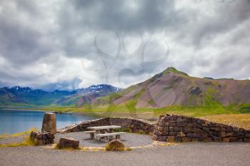 The table and benches for country picnic. Summer in Iceland. Multi-colored mountains surround lake with ice-blue water