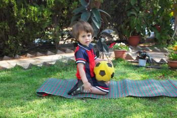 A lovely little boy resting on a green lawn with a yellow ball
