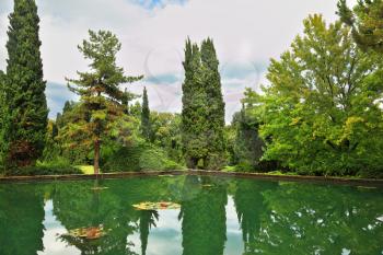  Magnificent Italian park at sunset. Smooth water of a pond reflects coastal cypresses and picturesque bushes