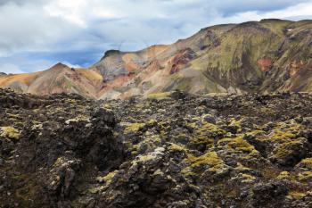 National Park Landmannalaugar in Iceland. Pieces of gray and black lava, sometimes covered with green moss. In the background - pink and orange rhyolite mountains