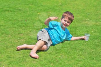 The charming four-year-old boy with pleasure has a rest on a green grassy lawn