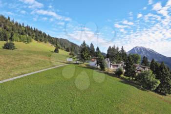 Swiss Alps. Road among green alpine meadow on the mountain side. Away - picturesque hotel