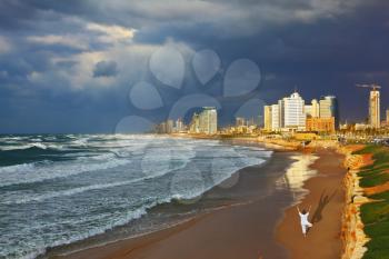 Storm cloud hanging over the sea, the woman in white performs yoga on one leg. Promenade and beach in Tel Aviv