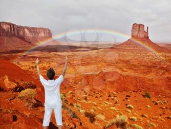 Navajo Reservation in the US. Red Desert and rocks - mitts sandstone. Woman in white performs asana Sun salutation under a huge rainbow