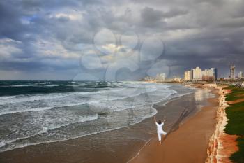 Storm cloud hanging over the sea, the woman in white performs asana Tree on one leg. Promenade and beach in Tel Aviv