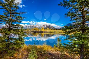 The coniferous forest at around lake. The concept of hiking. Mountains and scenic clouds are reflected in the water