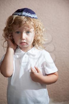 Autumn holiday of Sukkot. The charming little boy with long blond curls and blue eyes in the Jewish knitted yarmulke