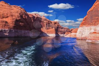 The foamy trace from powerboat crosses emerald waters. Hills from red sandstone surround the lake. The lake Powell on  river Colorado