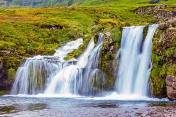 Mountains and falls. Cloudy day in Iceland. Cascade falls on the green grass mountain