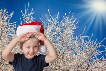 Cute three year old boy in a red cap of Santa Claus. Kid having fun smiling on the background of snow-covered forest