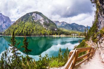 The footpath around the lake is fenced with a wooden handrail. Magnificent Alpine lake Lago di Braies. Concept of ecological and pedestrian tourism