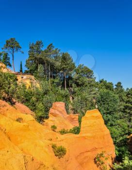 Unique red and orange hills in the province of Languedoc - Roussillon, France. Green trees create a beautiful contrast with the bright ocher