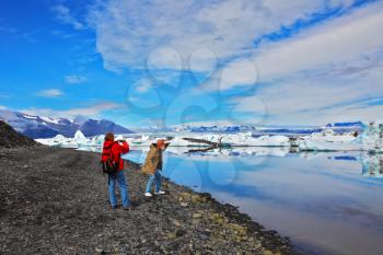ICE LAGOON, ICELAND - JULY 10, 2014: A couple of seniors tourists  walking and photographs on the banks of the lagoon Ice