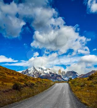 Concept of automobile extreme tourism. The gravel road in national park Torres del Paine. Mountains and rocks Torres are covered with snow and ice 