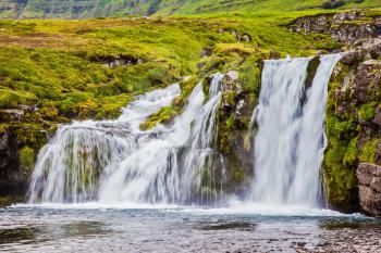 Summer in Iceland. At the foot of the mountain Kirkjoufell cascade falls Kirkjoufellfoss. Concept of exotic and extreme tourism